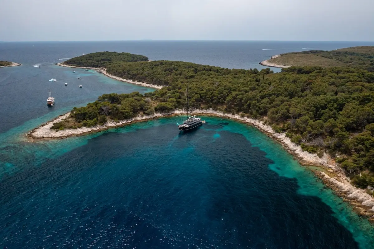 Aerial view of S/Y Rara Avis anchored in a sheltered cove ringed by pine-covered islands