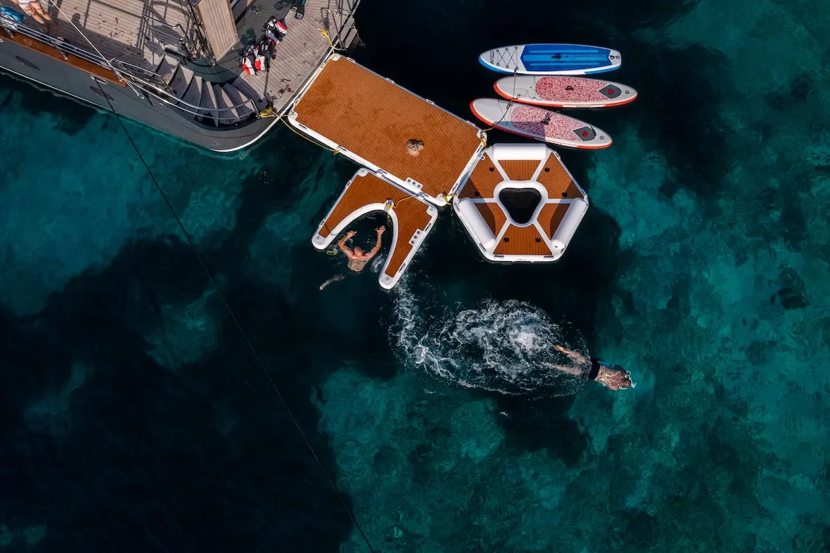 Guests swimming beside the swim platform, inflatable sea pool and paddleboards of S/Y Rara Avis