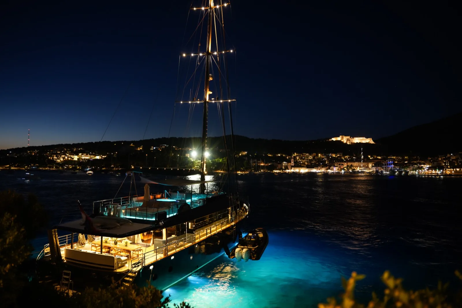 S/Y Rara Avis lit up at night in a bay below the old town fortress