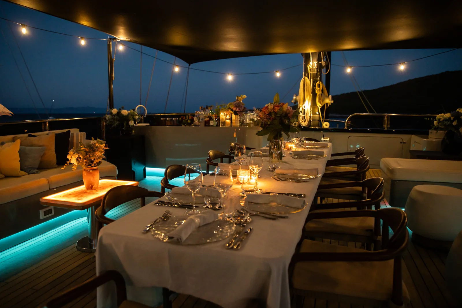 The sundeck dining table set for dinner at night under string lights