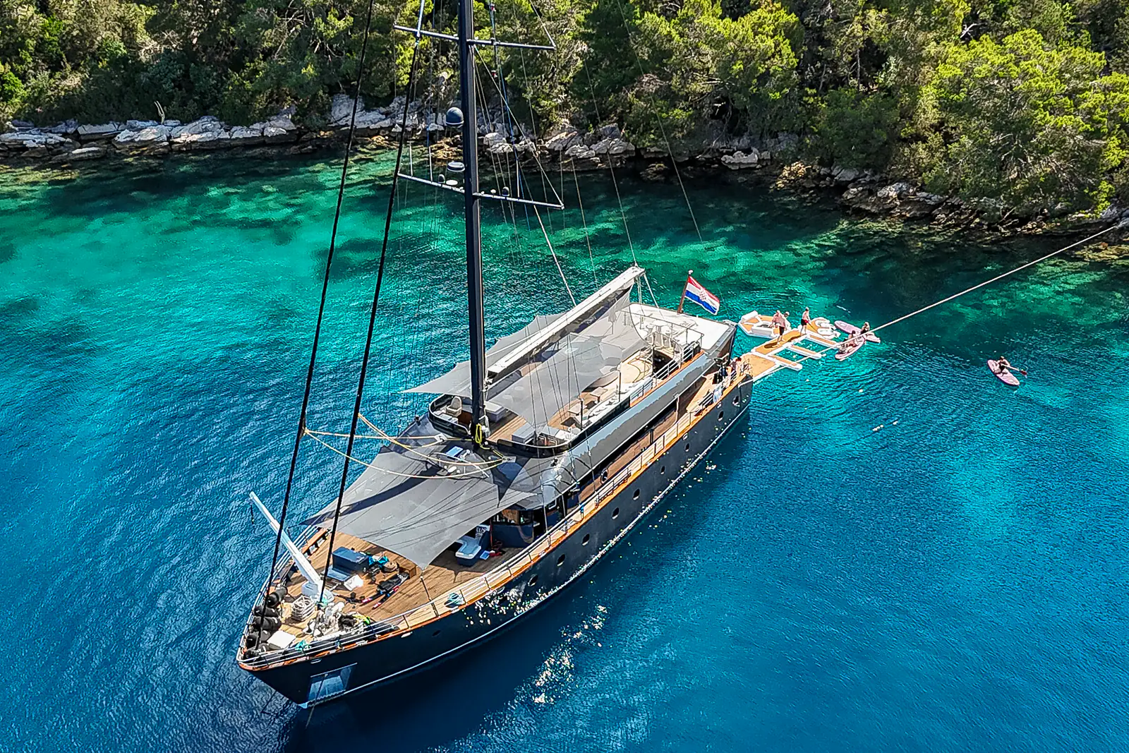 S/Y Rara Avis moored stern-to in a Croatian cove, guests on the floating swim platform