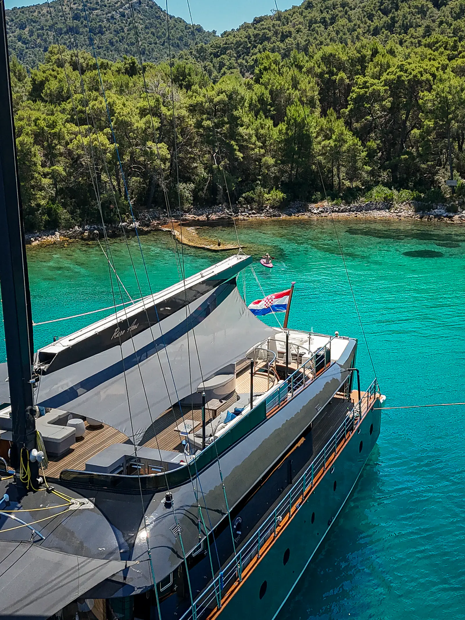 Sun deck of S/Y Rara Avis with the Croatian flag flying over a turquoise bay