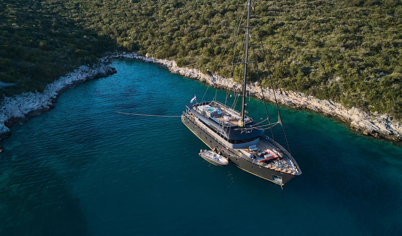 Dark-hulled sailing yacht Rara Avis resting in a hidden Croatian anchorage